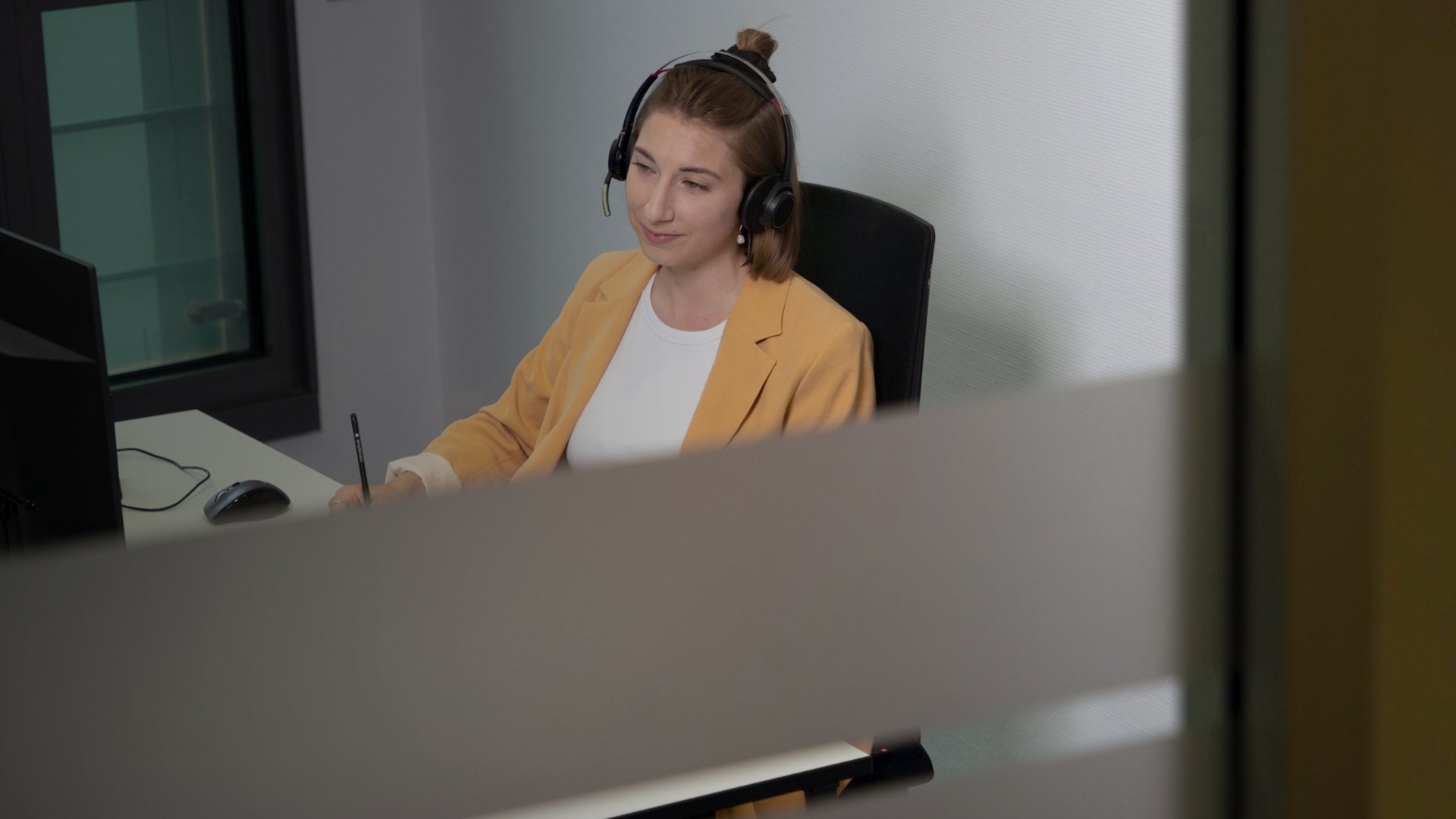 Frau sitzt am Schreibtisch mit Kopfhörern 